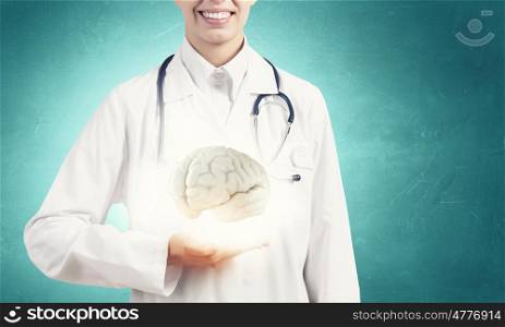 Mental health. Close up of female doctor with stethoscope and brain in hands