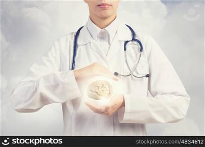Mental health. Close up of female doctor with stethoscope and brain in hands