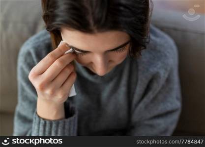 mental health, psychological problem and depression concept - sad crying woman with paper tissue sitting on sofa at home. crying woman with tissue sitting on sofa at home