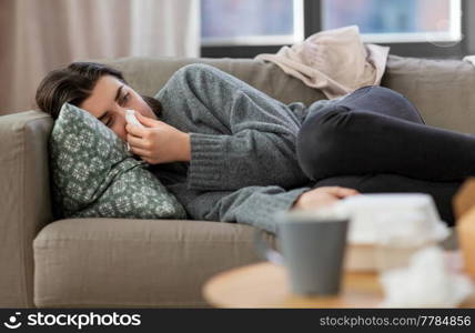mental health, psychological problem and depression concept - sad crying woman with paper tissue lying on sofa at home. sad crying woman with tissue lying on sofa at home