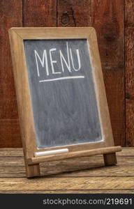 menu word in white chalk handwriting on a blackboard, copy space below against rustic barn wood