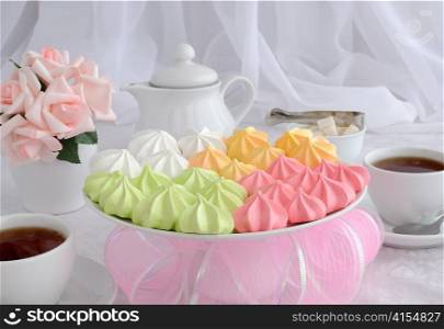 Meringue cookies of different colors on a plate with a cup of coffee
