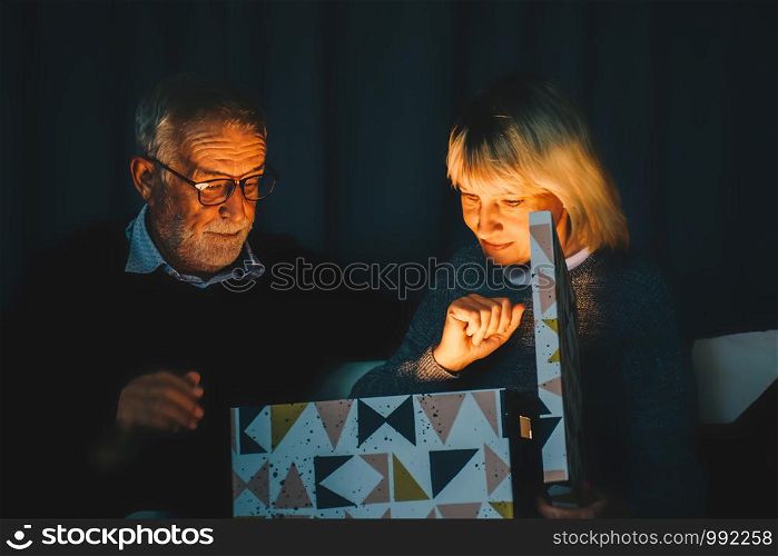 Merry Christmas and Happy Holidays.Senior couple opens the magic box with light in dark on Christmas day at home.Christmas family .