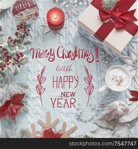 Merry Christmas and Happy New Year text on blue knitted blanket with red vintage Christmas decoration, present gift box, burning candles and cup of cappuccino . Top view. Flat lay. Greeting card