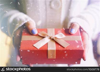 Merry Christmas concept, woman hands in winter clothes holding red gift box for surprising in snow background, holiday and festive