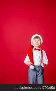 Merry Christmas. Cute cheerful little boy in Santa Claus hat on red background. A happy childhood with dreams and gifts. Close-up of baby&rsquo;s open mouth, milk tooth fell out.. Merry Christmas. Cute cheerful little boy in Santa Claus hat on red background.