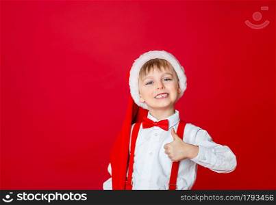 Merry Christmas. Cute cheerful little boy in Santa Claus hat on red background. A happy childhood with dreams and gifts. Close-up of baby&rsquo;s open mouth, milk tooth fell out.. Merry Christmas. Cute cheerful little boy in Santa Claus hat on red background.