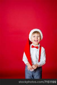 Merry Christmas. Cute cheerful little boy in Santa Claus hat on red background. A happy childhood with dreams and gifts. Close-up of baby?s open mouth, milk tooth fell out.. Merry Christmas. Cute cheerful little boy in Santa Claus hat on red background.