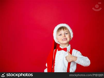 Merry Christmas. Cute cheerful little boy in Santa Claus hat on red background. A happy childhood with dreams and gifts. Close-up of baby?s open mouth, milk tooth fell out.. Merry Christmas. Cute cheerful little boy in Santa Claus hat on red background.
