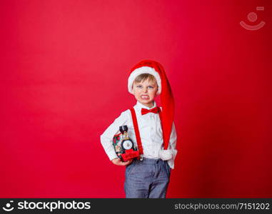 Merry Christmas. Cute cheerful little boy in Santa Claus hat on red background. A happy childhood with dreams and gifts. Close-up of baby?s open mouth, milk tooth fell out.. Merry Christmas. Cute cheerful little boy in Santa Claus hat on red background.