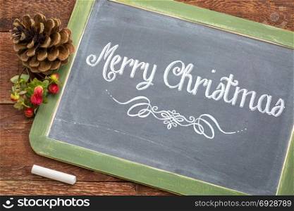 Merry Christmas greeting card - white chalk text on a vintage slate blackboard with a pine cone