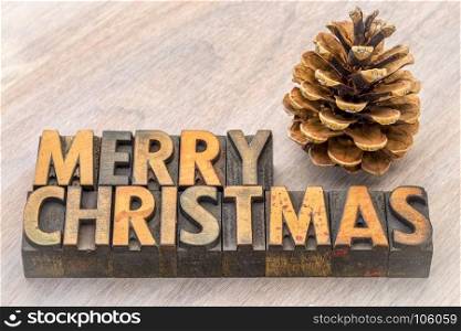Merry Christmas greeting card - word abstract in vintage letterpress wood type with a pine cone