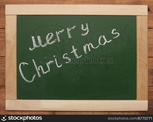 ""Merry Christmas" handwritten with white chalk on a blackboard"