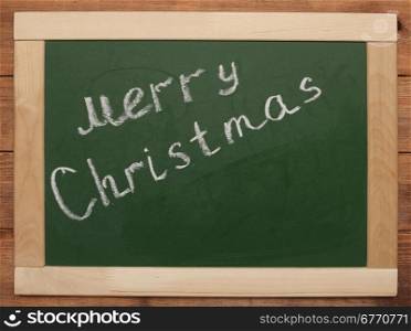 ""Merry Christmas" handwritten with white chalk on a blackboard"