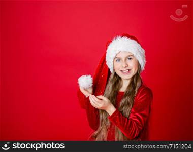 Merry Christmas, happy attractive girl in Santa?s hat on bright red bright color background. Portrait of a beautiful girl in anticipation of the New Year. Copy space.. Portrait of a beautiful girl in anticipation of the New Year. Copy space.
