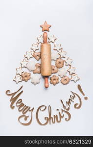 Merry Christmas lettering ,holiday tree made with rolling pin, cookies and gingerbread on white background, top view. Festive layout or pattern for greeting card