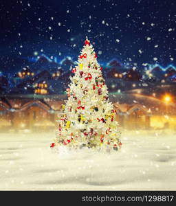 Merry christmas, snowy xmas tree with decoration, village on background, new year. Winter holiday celebration