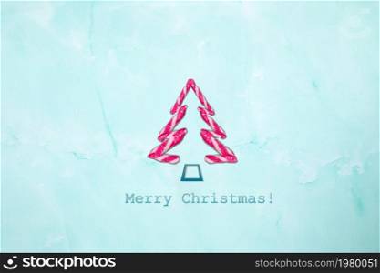 Merry Christmas text and shape Christmas tree of candy canes on light blue background. New Year winter composition, Holiday, Xmas, greeting card concept
