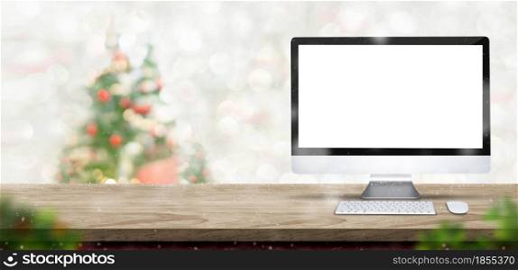 Merry Christmas with blank desktop computer on wood table at blur bokeh xmas tree decor with string light background,Winter banner backdrop for holiday greeting card advertise promotion on online