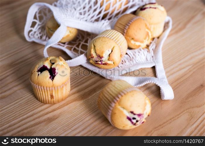 Mesh bag and delicious cupcakes on wooden background