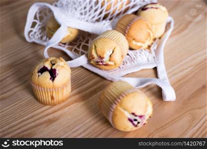 Mesh bag and delicious cupcakes on wooden background