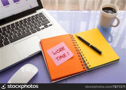 Message on paper with word WORK TIME ! on note stick on colorful book with laptop and a cup of coffee on glass table, top view image