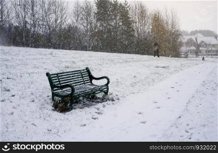 Metal bench in the park with snow covering in WInter, A lonely green bench at the public park with snowing in gloomy day