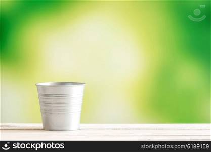 Metal bucket on a wooden desk on green background