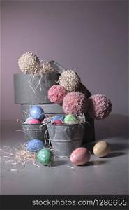 Metal buckets filled with painted easter eggs surrounded by some more eggs and round boxes with pompom balls in the back. Easter holiday and decoration concept.. Buckets filled with easter eggs with round boxes and pompom balls