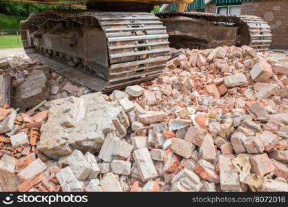 Metal caterpillars on heap of broken bricks of demolished house