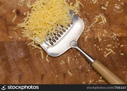Metal cheese grater and cheese on wooden cutting board, close-up. Metal cheese grater and cheese on wooden cutting board,