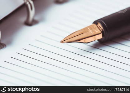 Metal feather pen on the ruled paper in the notebook