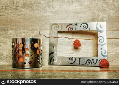 Metal frame with clematis fruits and candlestick with orange candle on a gray wooden background. Still life with metal and clematis
