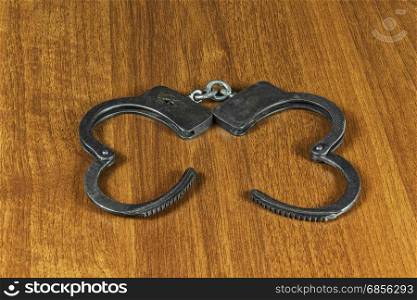 Metal handcuffs lie on the wooden surface