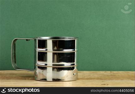 metal jug on old wooden table over green background