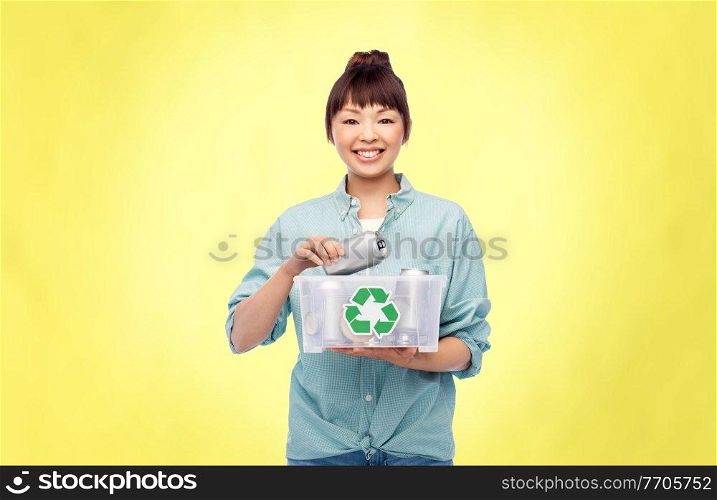 metal recycling, waste sorting and sustainability concept - smiling young asian woman holding plastic box with tin cans over illuminating yellow background. smiling young asian woman sorting metallic waste