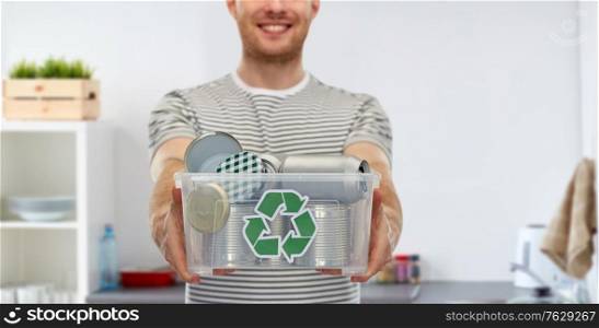 metal recycling, waste sorting and sustainability concept - smiling young man in striped t-shirt holding plastic box with tin cans over home kitchen background. smiling young man sorting metallic waste