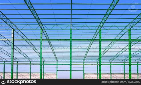 Metal roof beam and columns of new industrial factory building outline structure in construction area against blue sky background, symmetric view