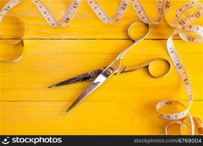 Metal scissors and measure tape on yellow background. Fashion industry concept.