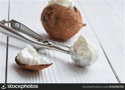 Metal scoop with fresh coconut ice cream on a light wooden background. Coconut ice cream in a metal spoon