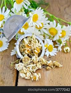 Metal sieve with dried chamomile flowers, fresh flowers daisies on a background of wooden boards
