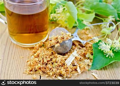 Metal sieve with dried flowers of lime, fresh flowers linden, tea in glass mug on a wooden board