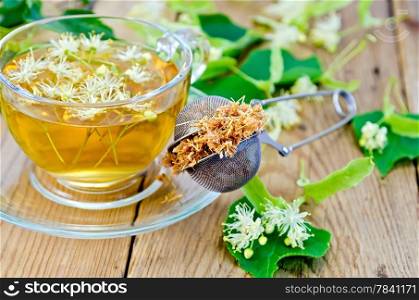 Metal sieve with dried flowers of lime, fresh flowers linden, tea in glass cup on the background of wooden boards