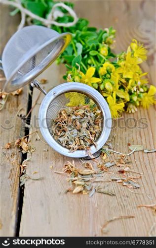 Metal strainer with dry flowers tutsan, fresh flowers tutsan against a wooden board