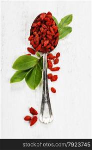 Metal tablespoon of dried goji berries on wooden background