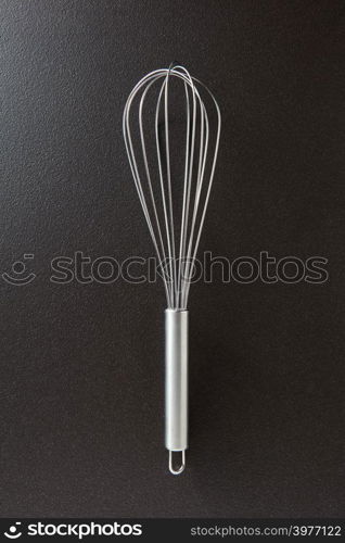 Metal whisk presented on a black concrete background with space for text.. Kitchen device for cooking different foods. Top view. Kitchen metal beater on a black concrete background with copy space. Kitchen appliance for cooking. Top view