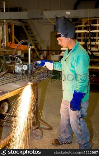 Metal worker in a factory using a track burner to cut a piece of metal. Authentic and accurate content depiction with all work being performed according to industry code and safety standards.