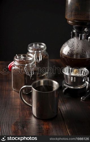 Metallic cup and vacuum coffee maker also known as vac pot, siphon or syphon coffee maker and coffee glass containers on rustic wooden table