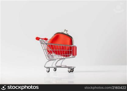 Metallic shopping cart trolley and Red Coin Purse on light gray background with copy space. Shopping symbol