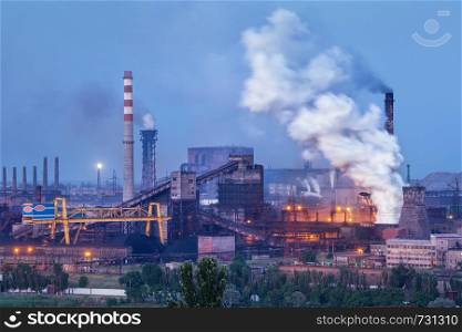 Metallurgical plant with white smoke at night. Steel factory with smokestacks . Steelworks, iron works. Heavy industry. Air pollution from smokestacks, ecology problems. Industrial landscape at twilight